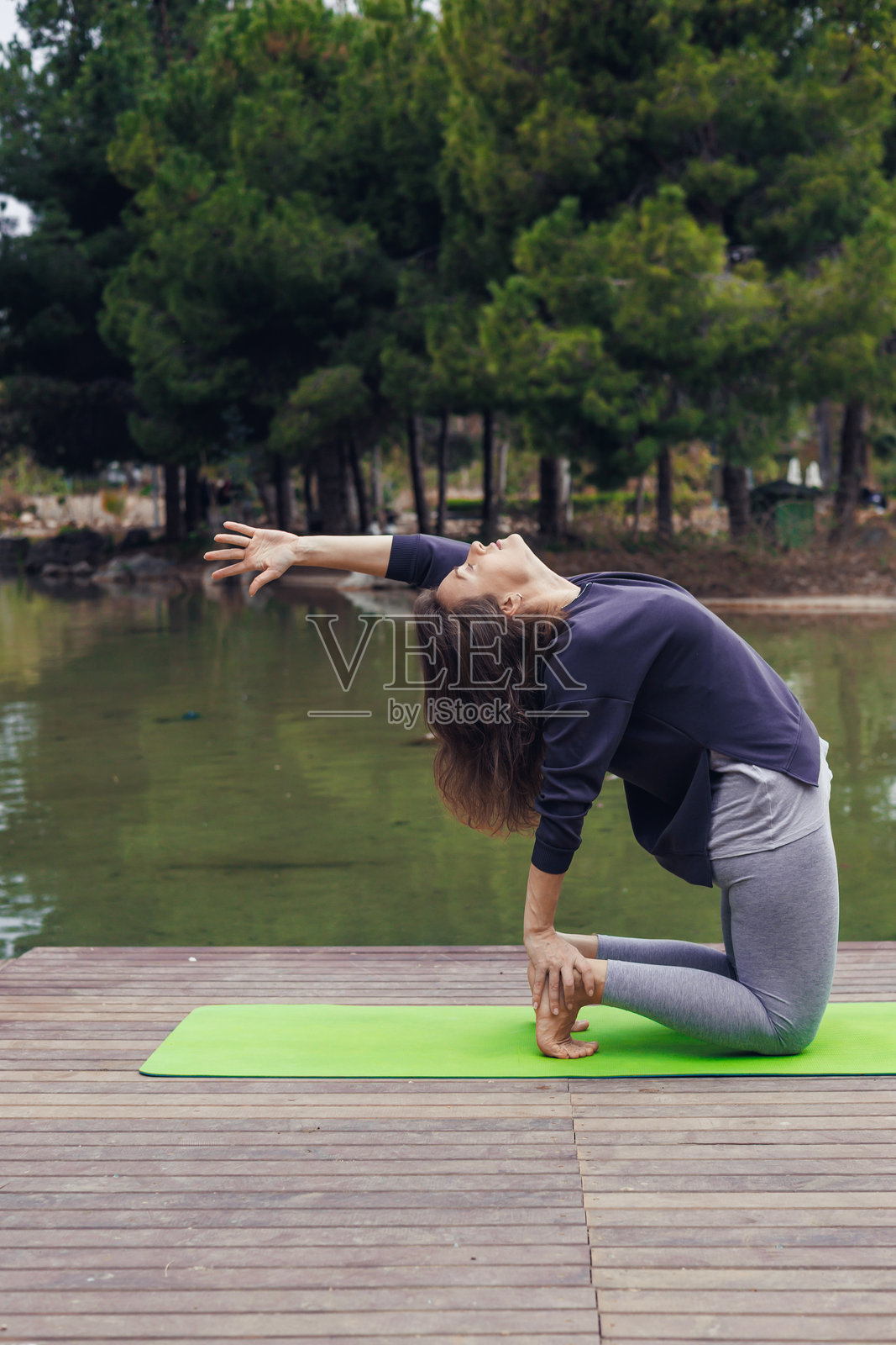 一位白人女性在树木环绕的宁静湖边垫子上练习瑜伽。她处于深拉伸姿势，专注于呼吸。照片摄影图片