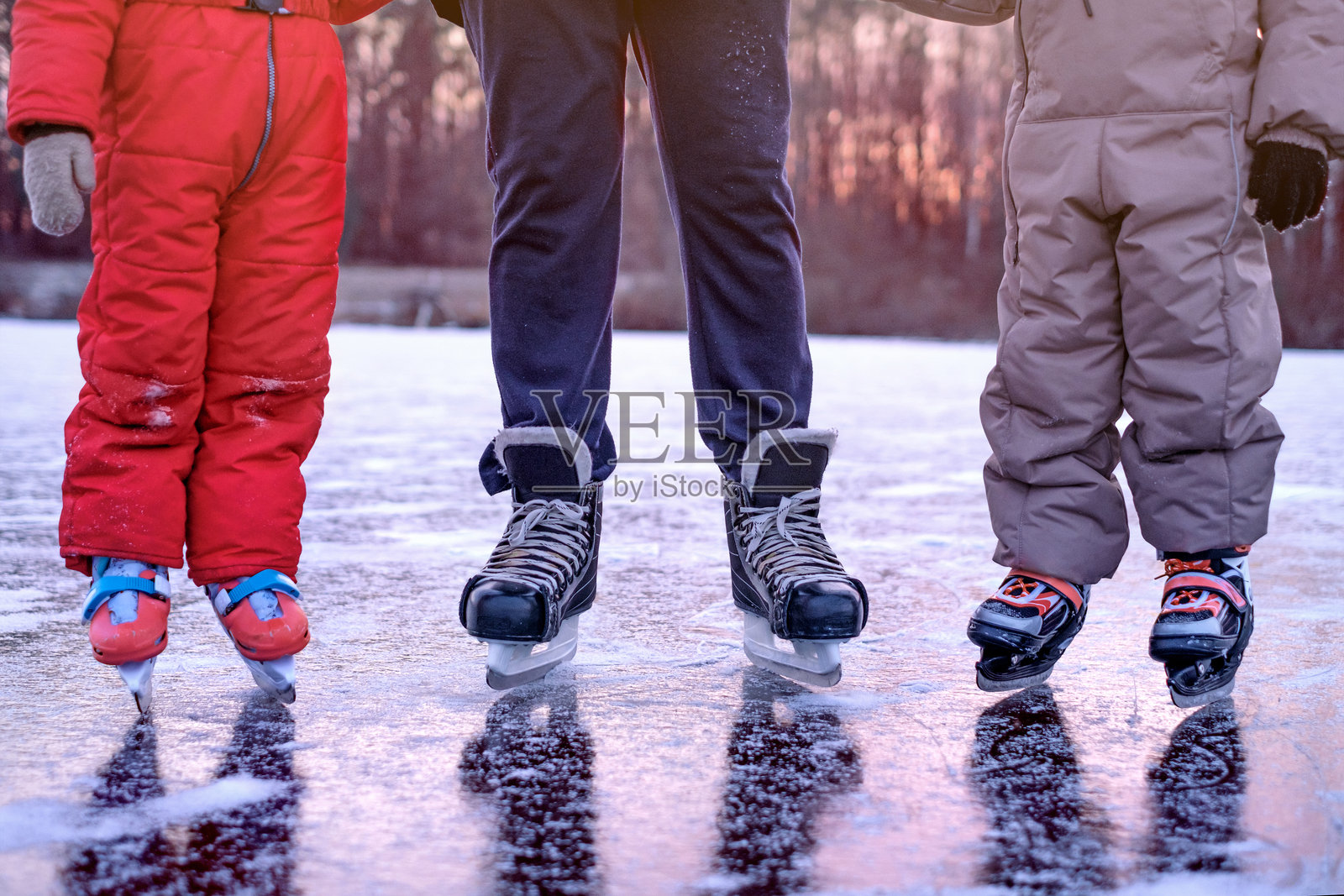 日落黄昏时，孩子们和爸爸的溜冰鞋在冰封湖面的冰上特写照片摄影图片