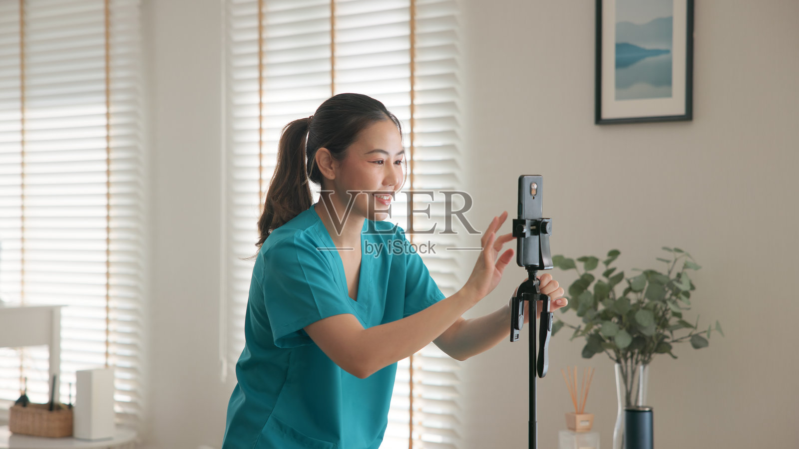 年轻的亚洲Z世代女性，抗衰老专家，现代护士，正在通过手机应用直播、拍摄视频自拍，从事线上副业，作为一名亚洲数字虚拟博主进行拍摄，关注心理健康护理。照片摄影图片