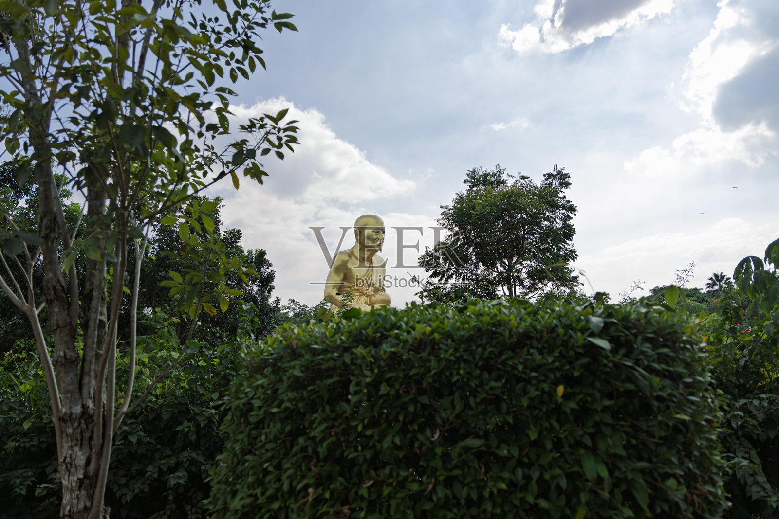 泰国考艾露普托特寺公园户外金色坐姿佛像，周围绿树环绕，天空多云照片摄影图片