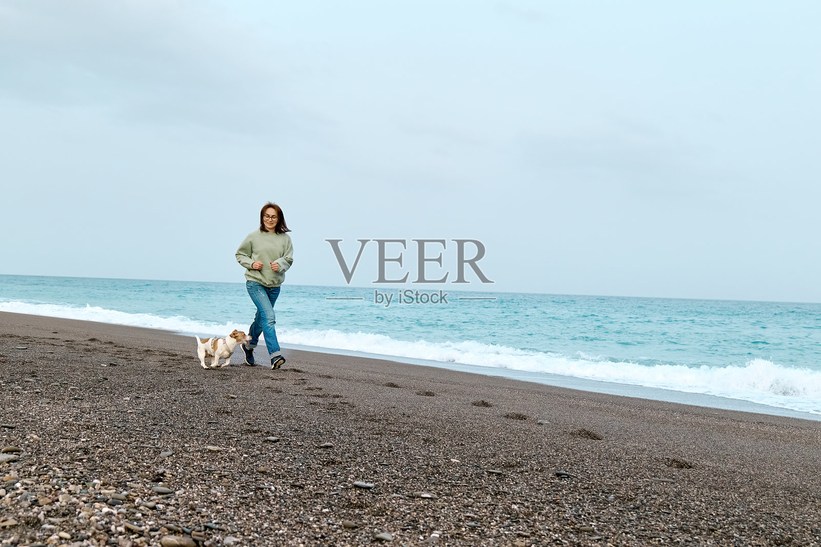 一位女士在中季节的沙滩上与她的杰克罗素梗犬共度时光，训练和玩耍。照片摄影图片