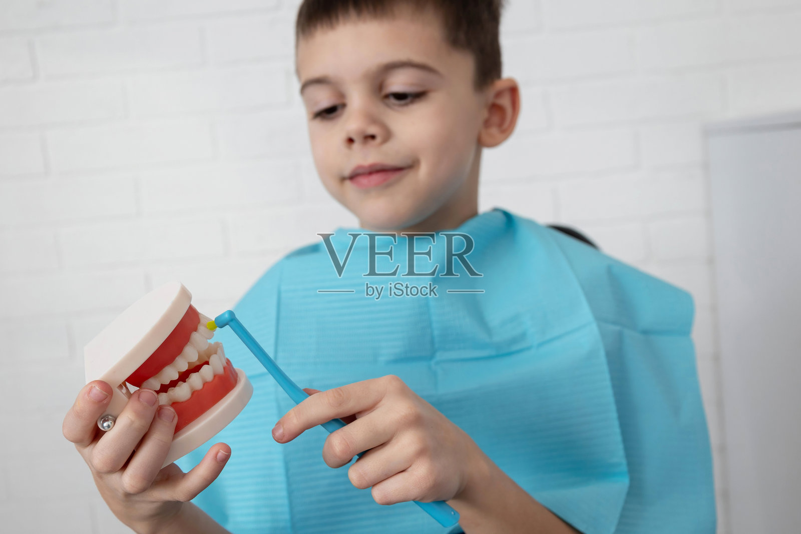 男孩在诊所对着牙齿模型刷牙，学习儿童口腔卫生照片摄影图片