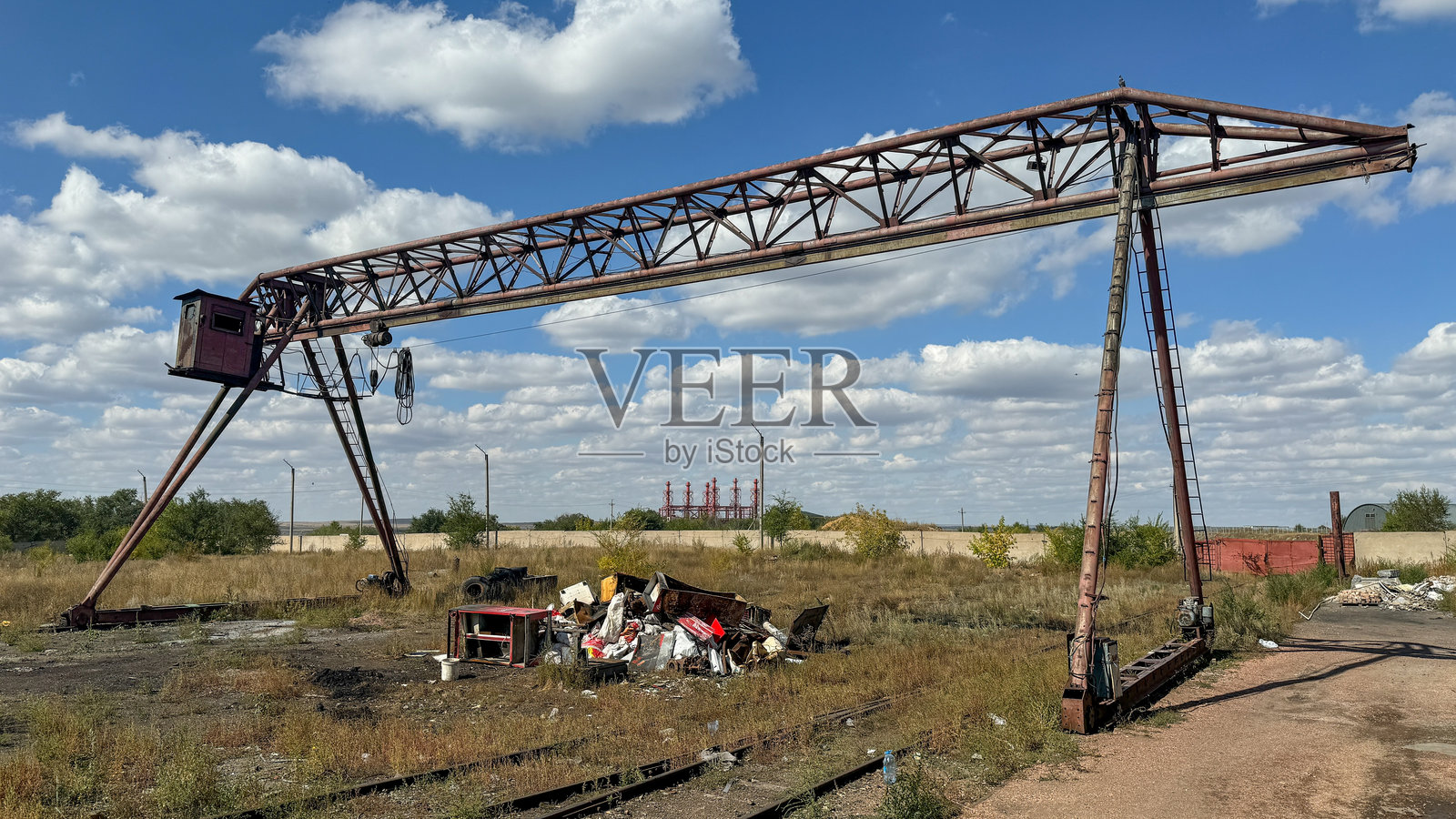 在蓝天阴云下，工业废料场里巨大的、老旧的、生锈的龙门起重机。照片摄影图片