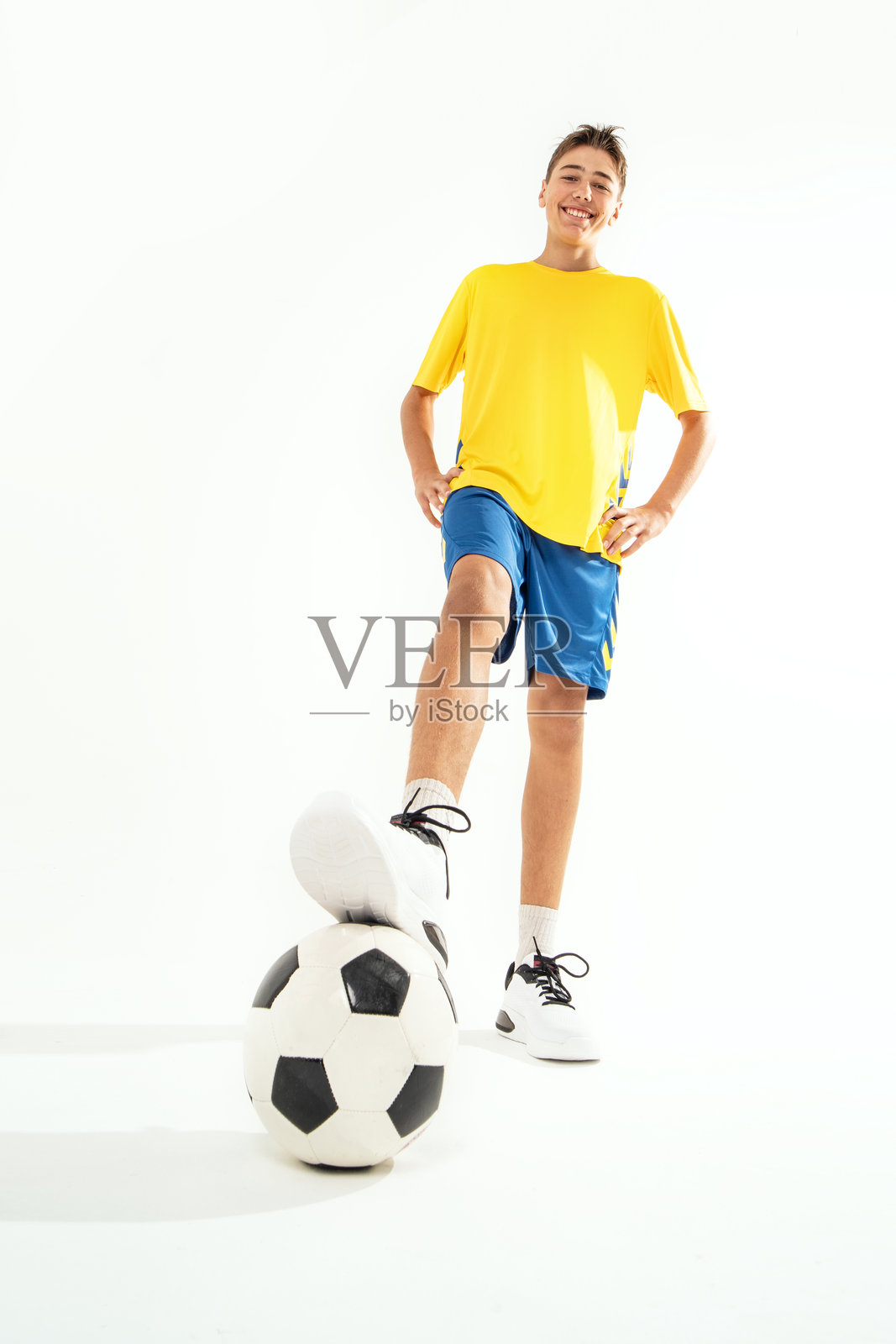 身穿运动服的微笑少年手持足球，在白色影棚背景前摆姿势。照片摄影图片