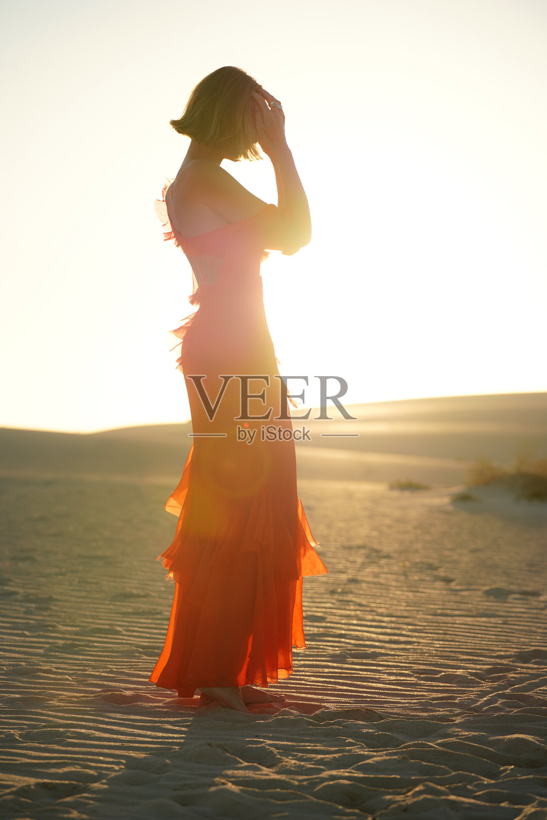 身着优雅红裙的女子走在沙漠沙丘的沙地上，享受放松的时光。照片摄影图片