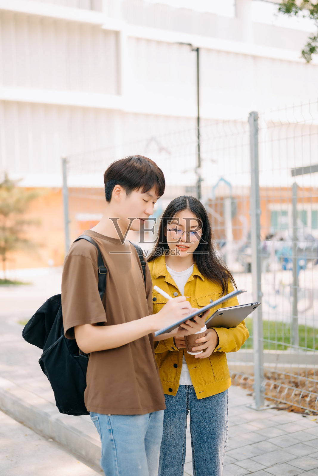 两位聪明的亚裔大学生正在专注地进行他们的学校项目，看着笔记本电脑和平板电脑，并进行讨论。照片摄影图片