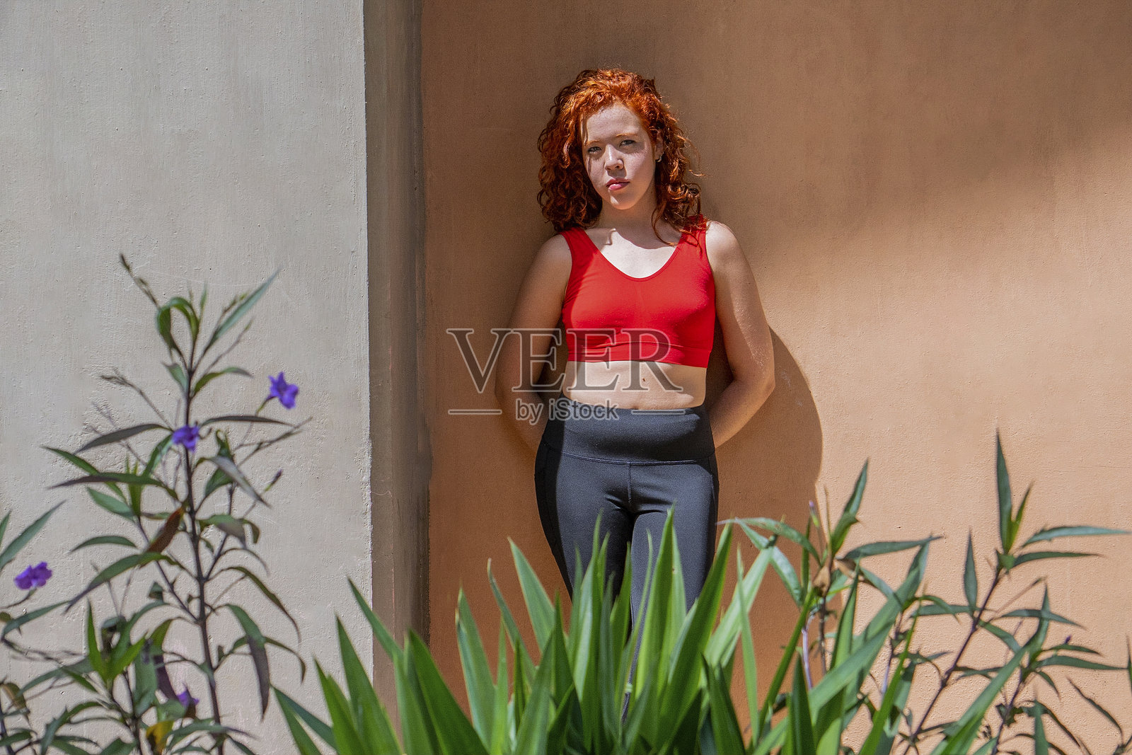 身穿红色背心和黑色裤子的女人站在墙前照片摄影图片
