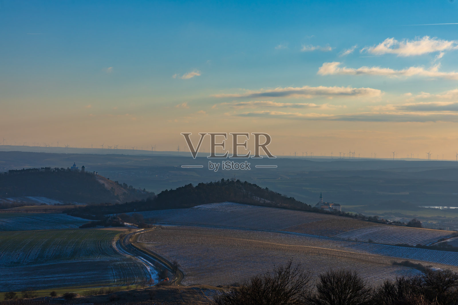 米库洛夫全景，地平线上有圣山和风力涡轮机。日落时分南摩拉维亚的冬季景观，带有薄薄的积雪。照片摄影图片