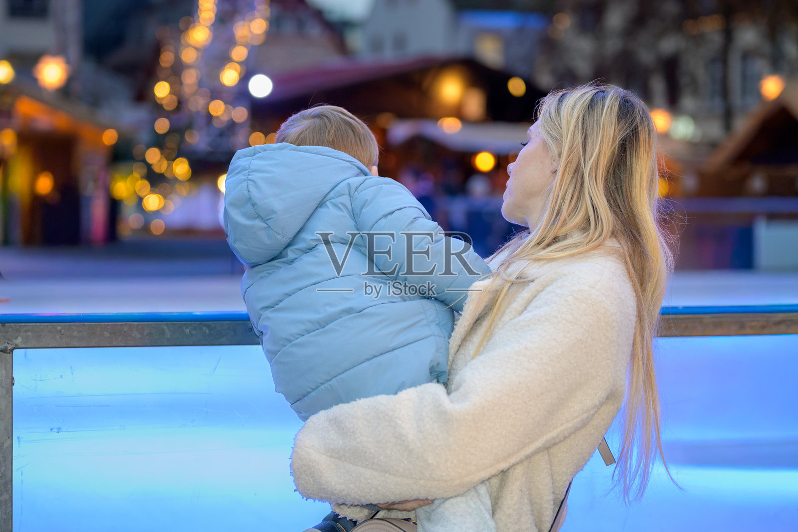 母亲在冬日集市上抱着蹒跚学步的孩子照片摄影图片