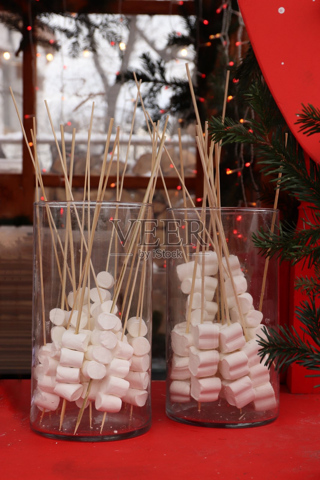 玻璃容器里的棉花糖串，摆放在红色桌子上，周围环绕着节日彩枝和花环照片摄影图片