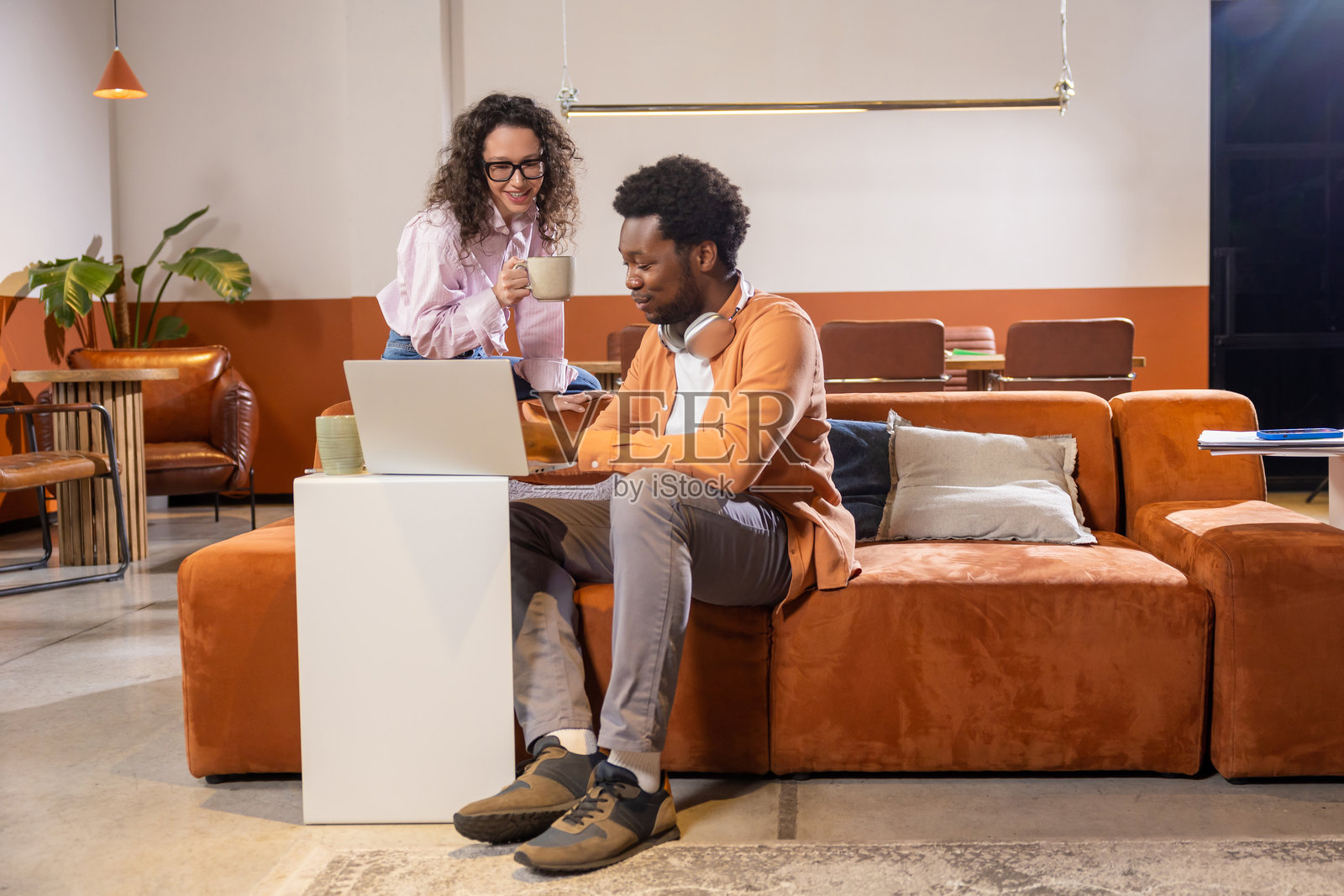 快乐的女士拿着饮料，在正在用笔记本电脑打字的男士旁边摆姿势照片摄影图片