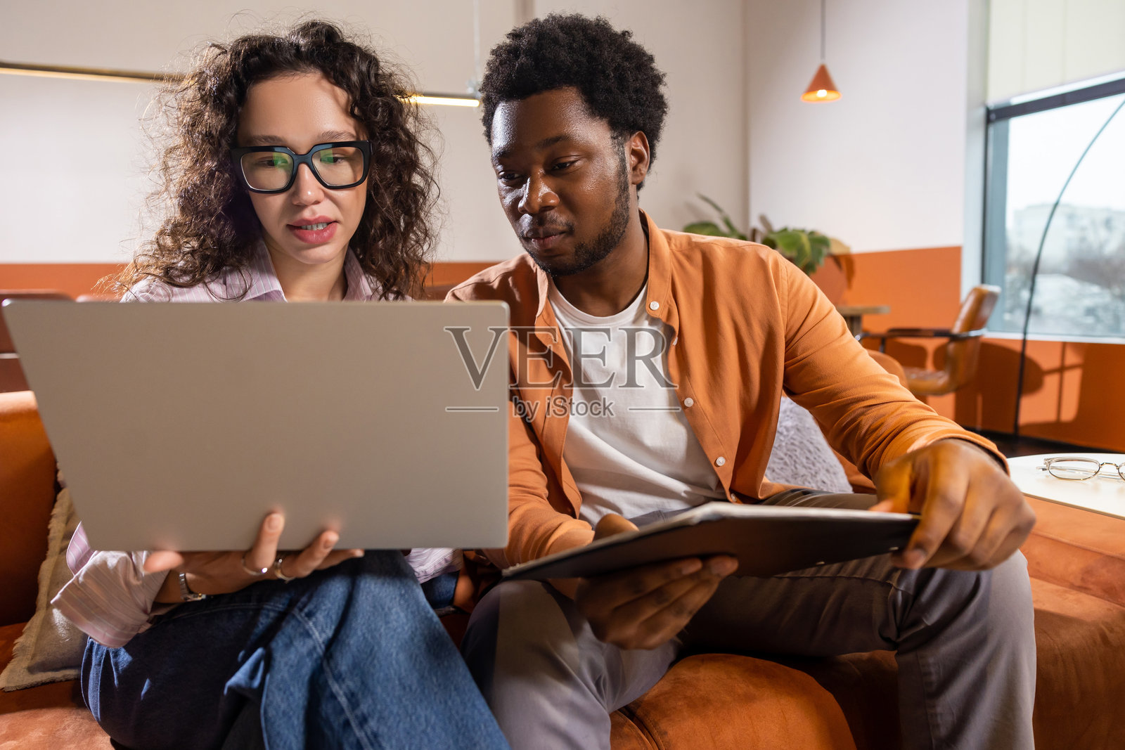 卷发女子与男子共用笔记本电脑和平板电脑协作工作照片摄影图片