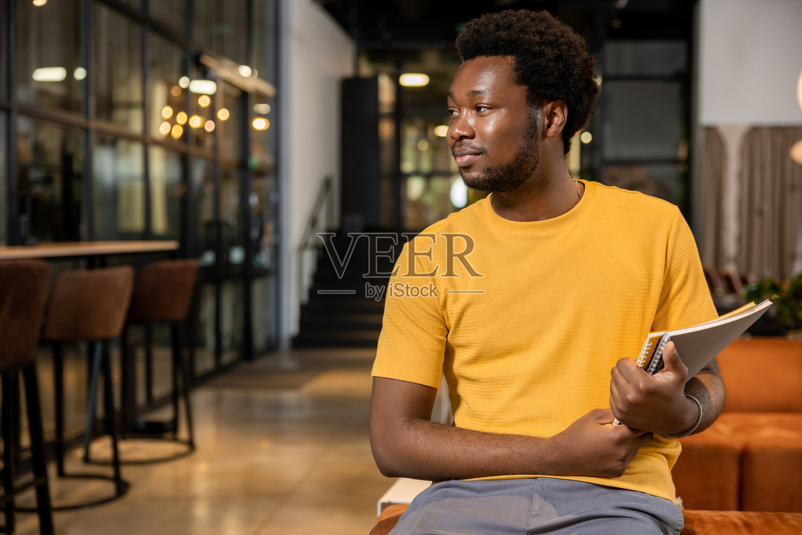 非裔美国男子在共享办公空间里放松地坐在橙色沙发上，手里拿着笔记本，面带微笑照片摄影图片
