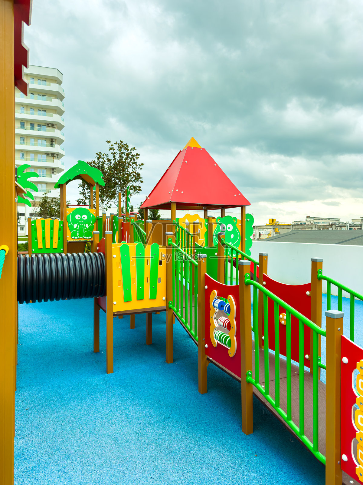 城市白天，灰色云层下的屋顶上，孩子们玩耍的彩色游乐设施，有绿色和红色的结构。照片摄影图片