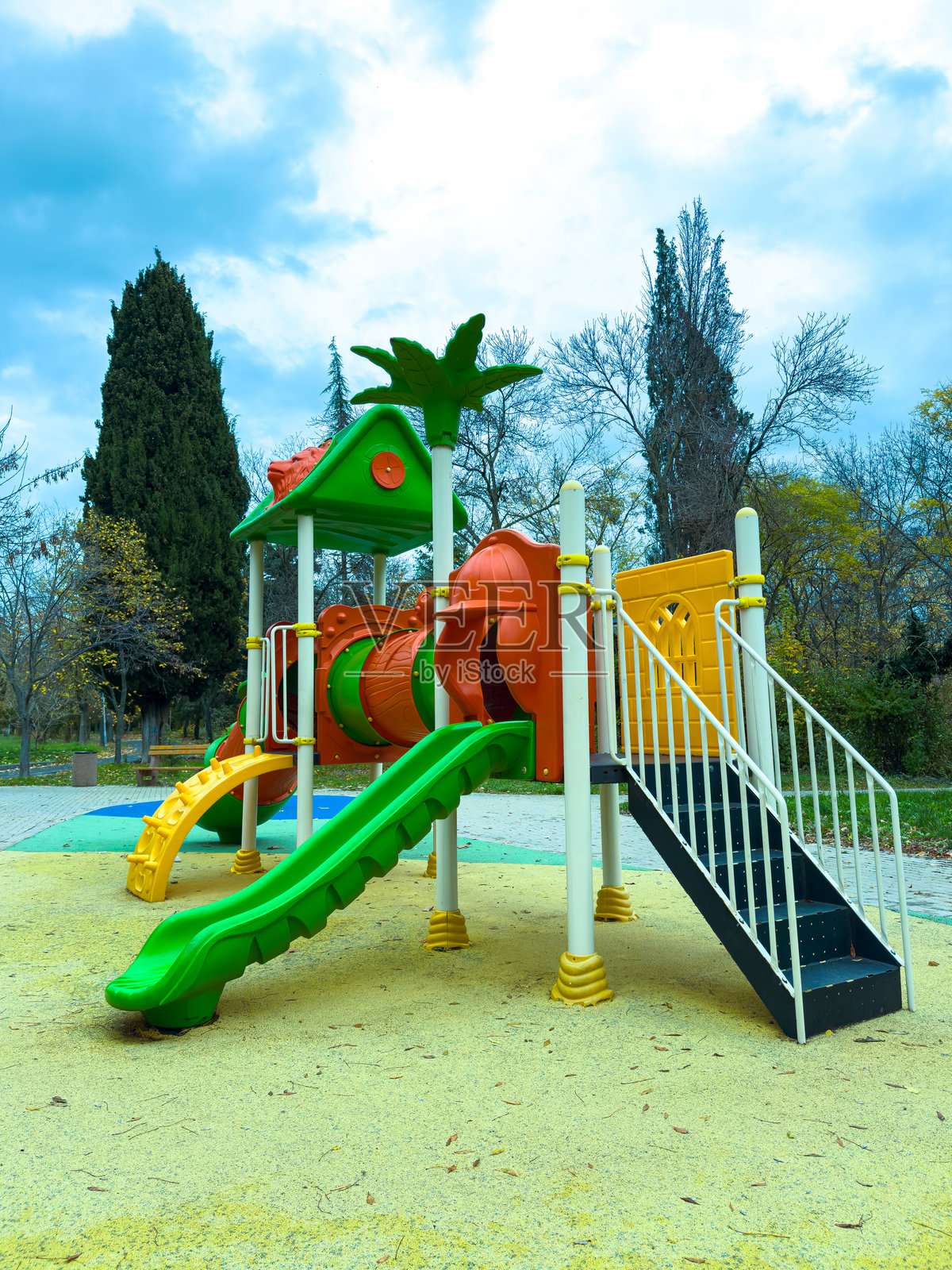明亮的游乐场设施，配有滑梯和隧道，坐落在公园里，树木环绕，天气多云照片摄影图片