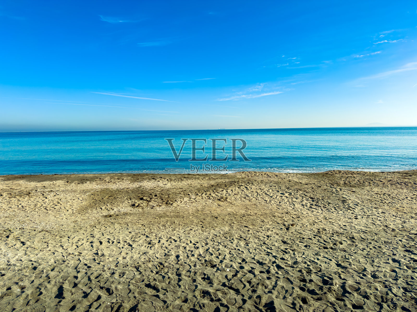 晴朗的蓝天白日，海岸边，明亮的蓝色海水与沙滩交汇，水面平静，沙滩宽阔。照片摄影图片