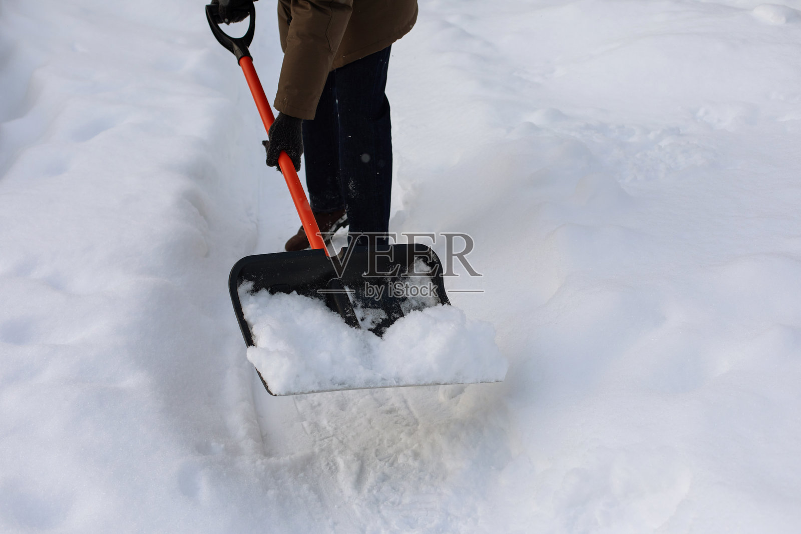 大雪过后，一名男子在户外用铲子铲除雪堆，清理冬季积雪的道路。照片摄影图片