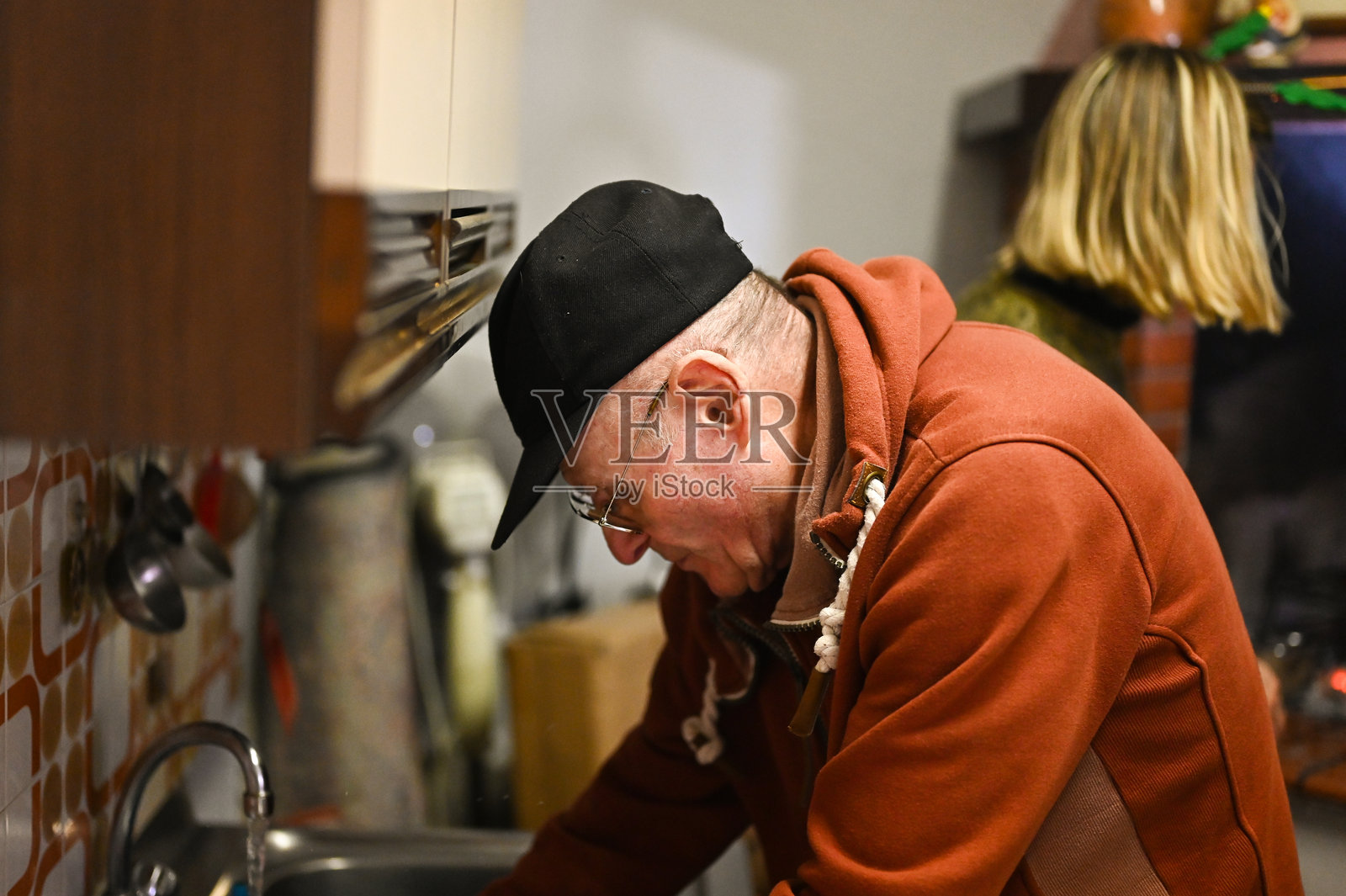 一位年长的男士正在厨房烹饪，一位女士处于模糊状态照片摄影图片