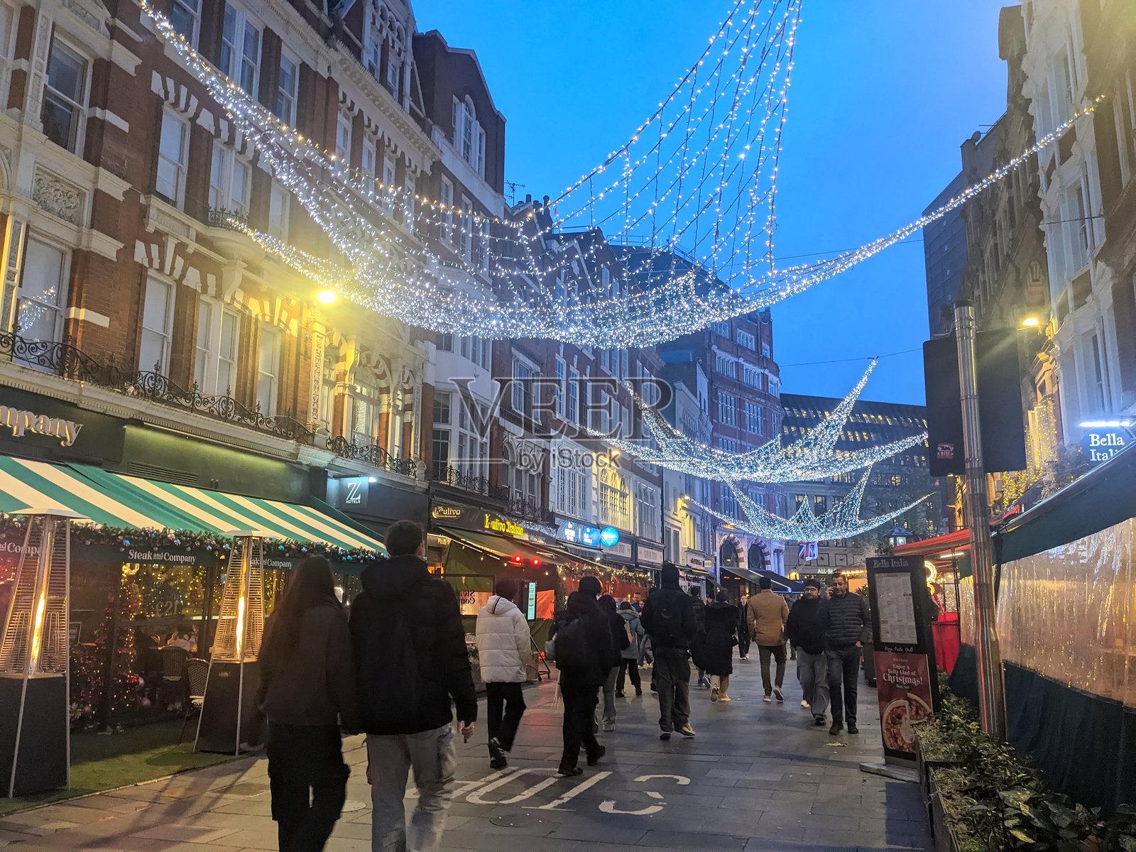傍晚时分,行人们走过伦敦欧文街,街道上装饰着节日的圣诞彩灯。照片摄影图片