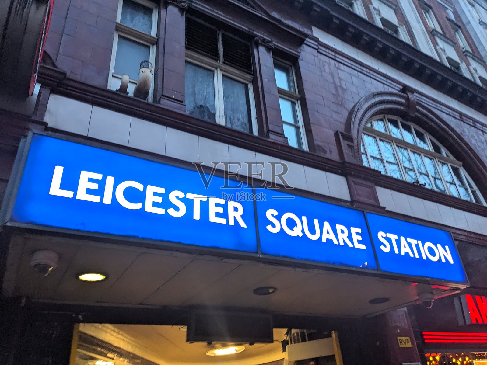 从低角度拍摄的、灯光照亮的、位于历史悠久的莱斯特广场地铁站入口处的蓝色标牌照片摄影图片