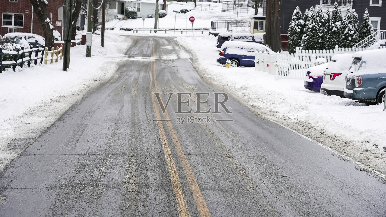 一场冬季风暴过后，道路上覆盖着积雪。房屋坐落在道路两侧，停放着汽车。照片摄影图片