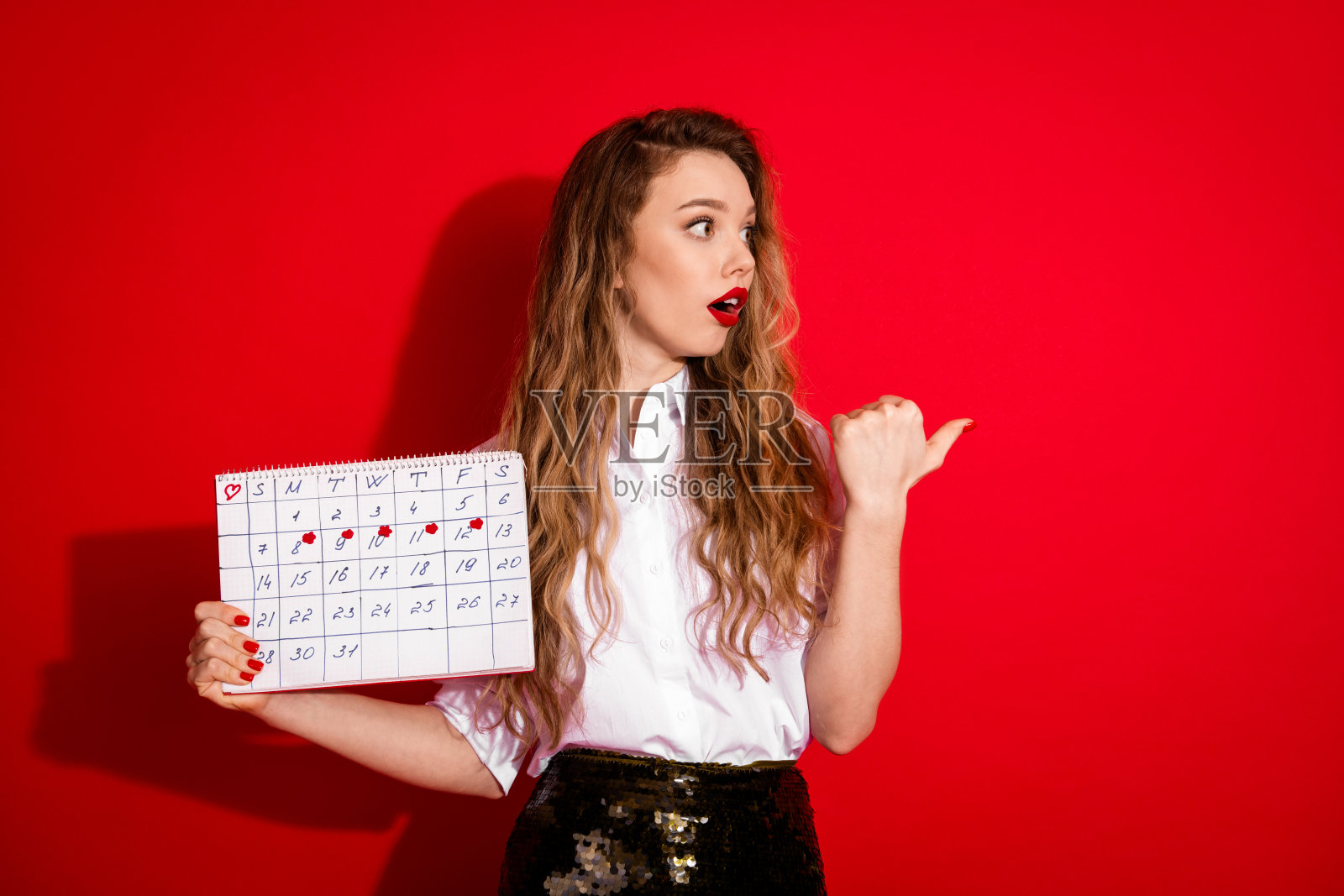 身着时尚服饰的女子手持日历，背景为红色，寓意规划与日程安排的概念。照片摄影图片