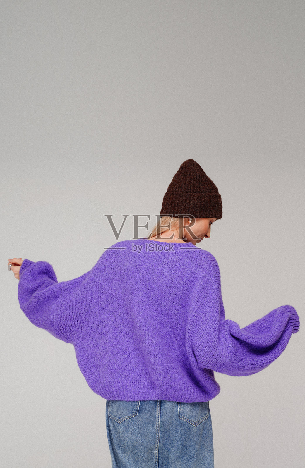 身穿时尚紫色毛衣和棕色帽子的女孩在工作室的灰色背景前摆姿势。照片摄影图片