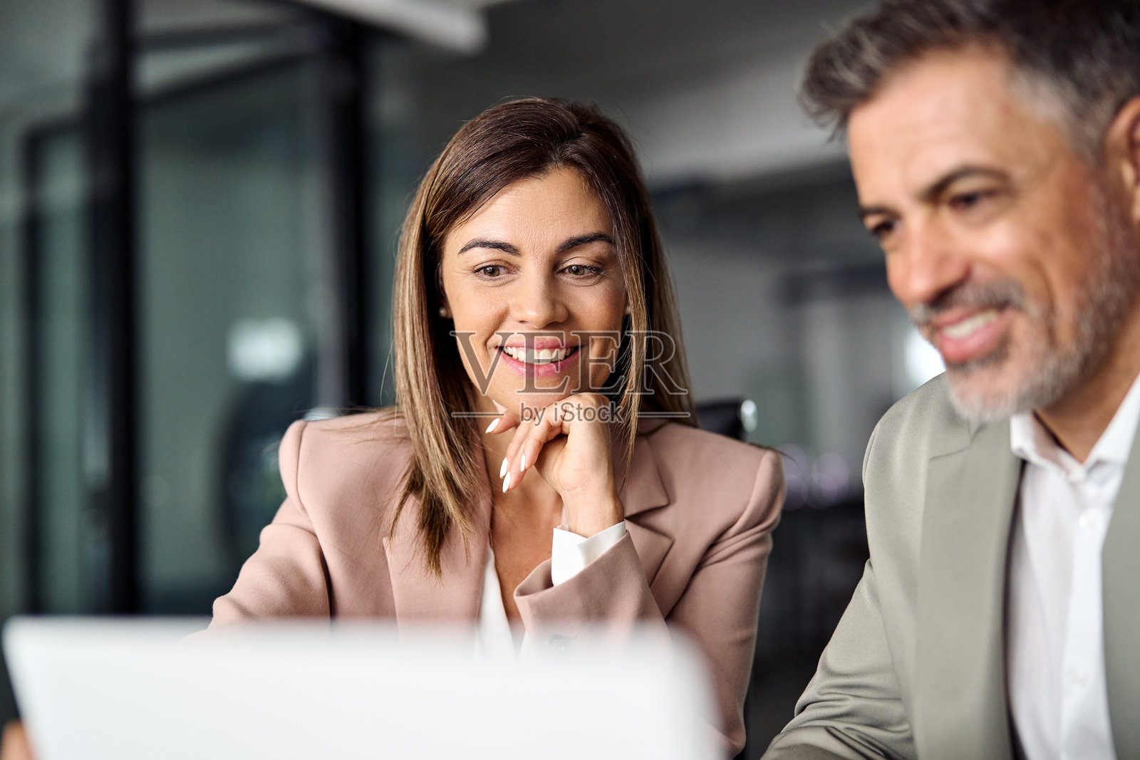 一位微笑的职业女性在办公室会议上使用笔记本电脑工作，旁边有一位男同事。照片摄影图片