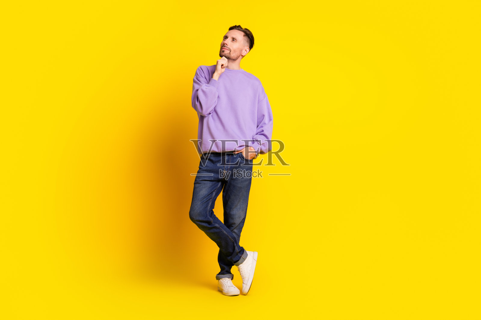 身穿紫色连帽衫的年轻男子，思绪万千，背景是明亮的黄色，展现了休闲时尚与生活方式照片摄影图片