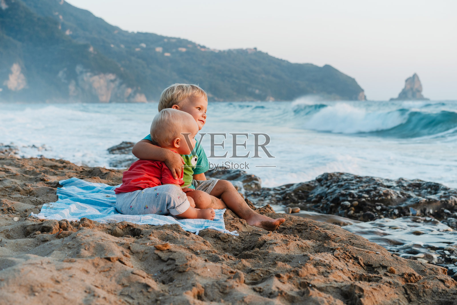 两个快乐的小孩坐在沙滩上望着大海。照片摄影图片