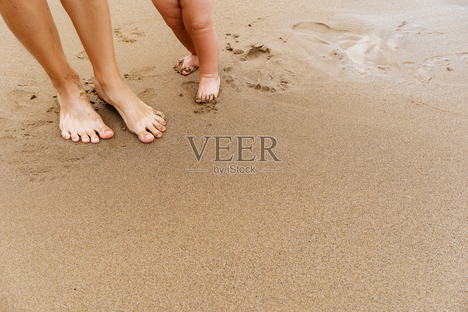 宝宝蹒跚学步。妈妈和小孩赤脚在海边沙滩上散步。照片摄影图片