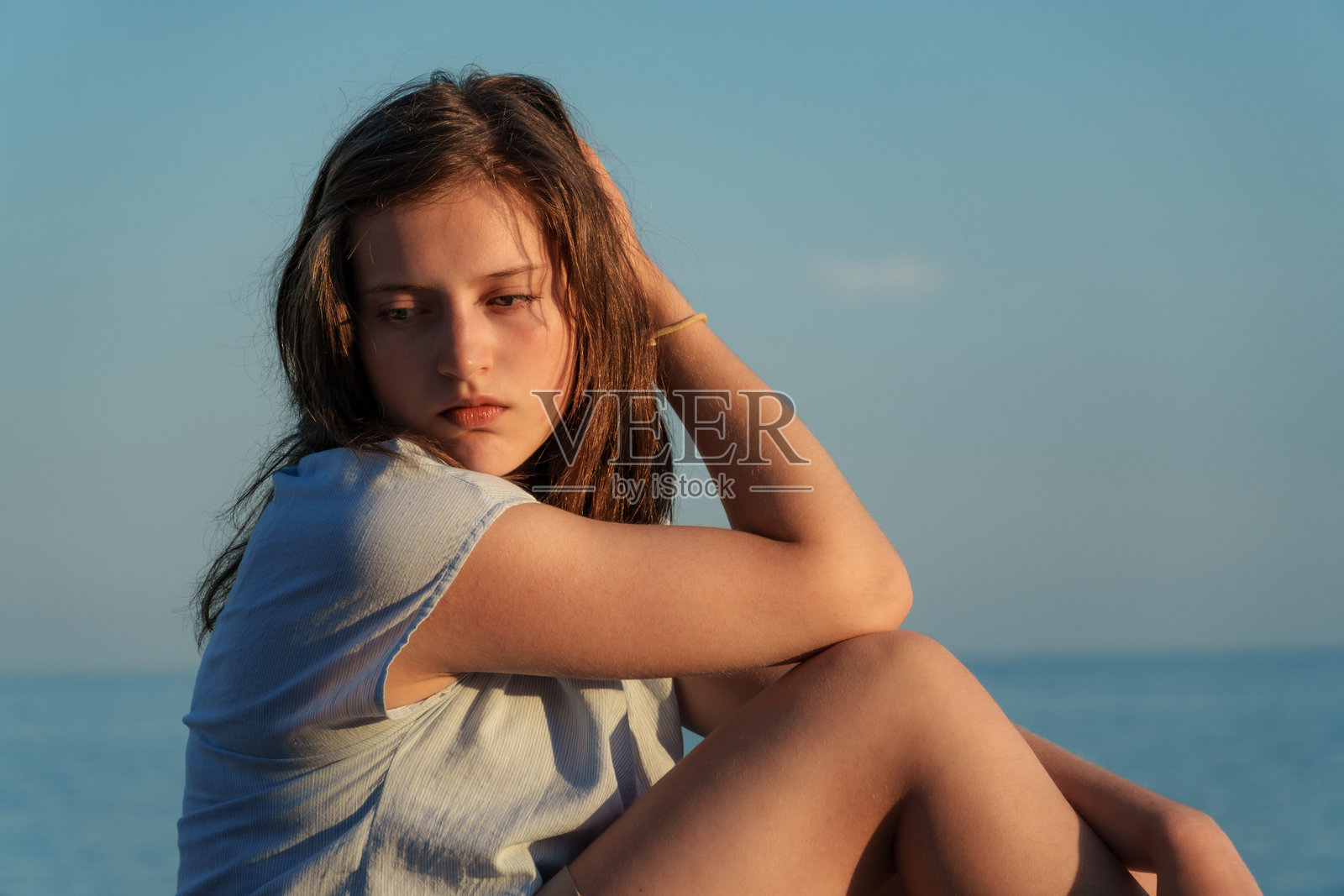 日落时分，一位年轻女子坐在海边，若有所思地看向远方，充满情感的夏日假期在黑山佩特罗瓦茨。照片摄影图片