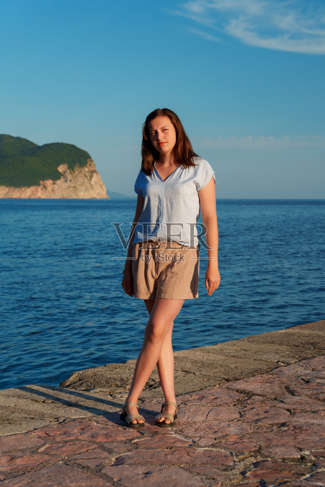 年轻女子身着休闲夏装，在黑山佩特罗瓦茨的海滨码头摆姿势，全身肖像，表情平静，地中海度假概念。照片摄影图片