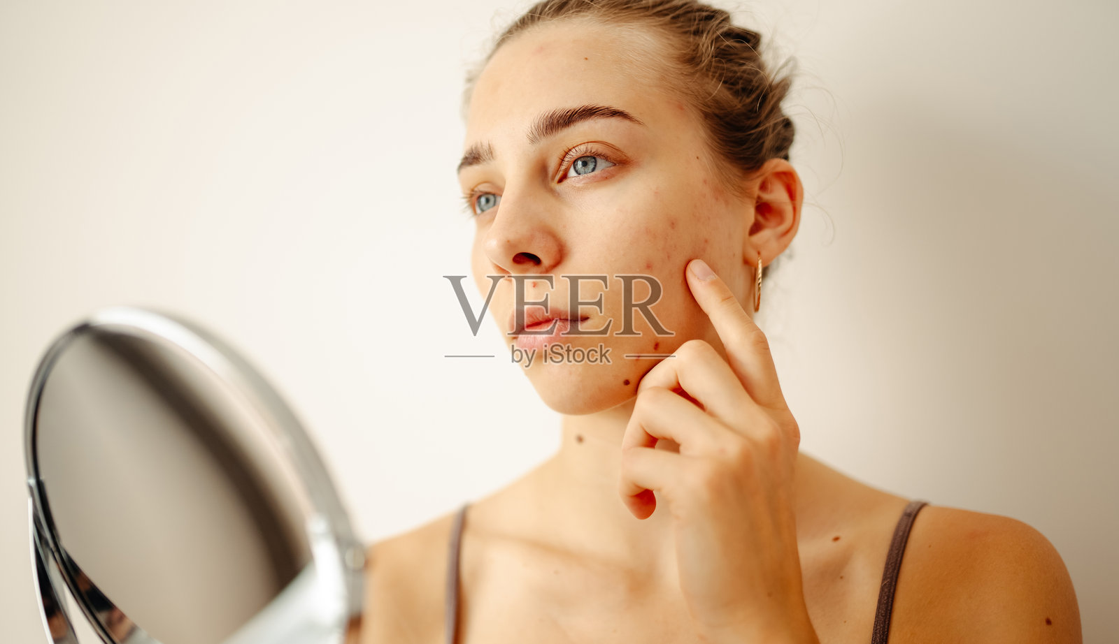 明亮的房间里，一个面部有瑕疵的年轻女子正凑近小镜子观察。照片摄影图片