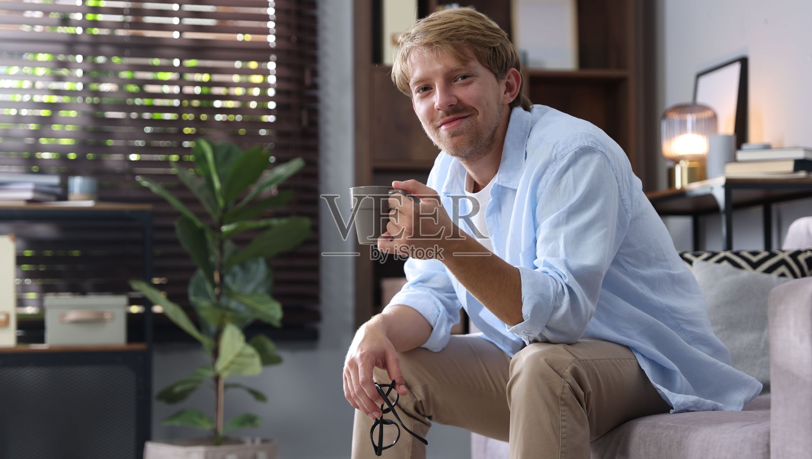 男人坐在家里的沙发上，手里拿着一杯饮料，留有文字空间照片摄影图片