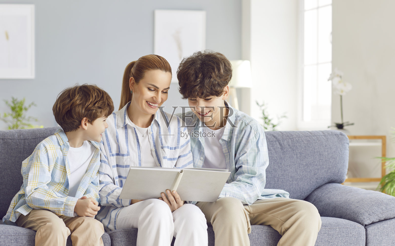 慈爱的母亲，一位关怀的女性，与年幼和青少年儿子一起观看相册中的照片照片摄影图片