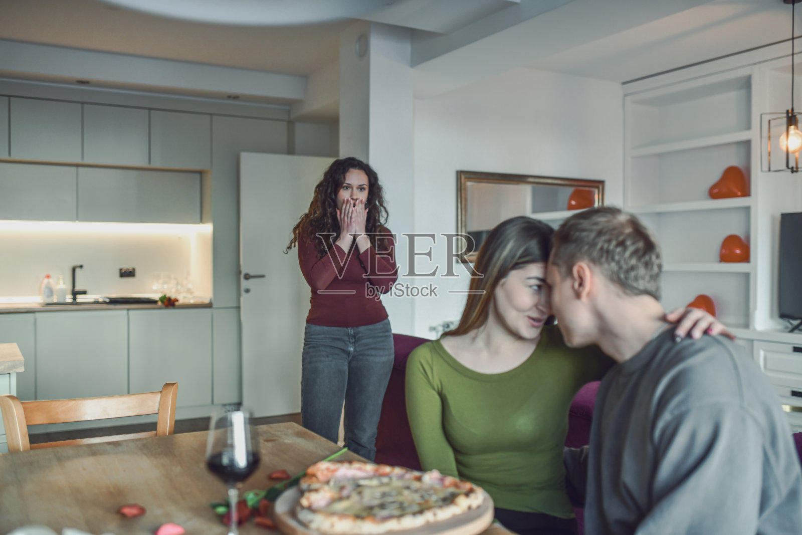 浪漫的家庭晚餐与披萨：在情人节，一对情侣在朋友惊讶的注视下窃窃私语照片摄影图片