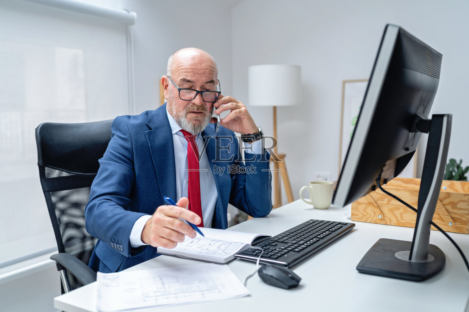 一位穿着西装、手持钢笔、在现代办公室用智能手机讲话的忧虑中年男士照片摄影图片