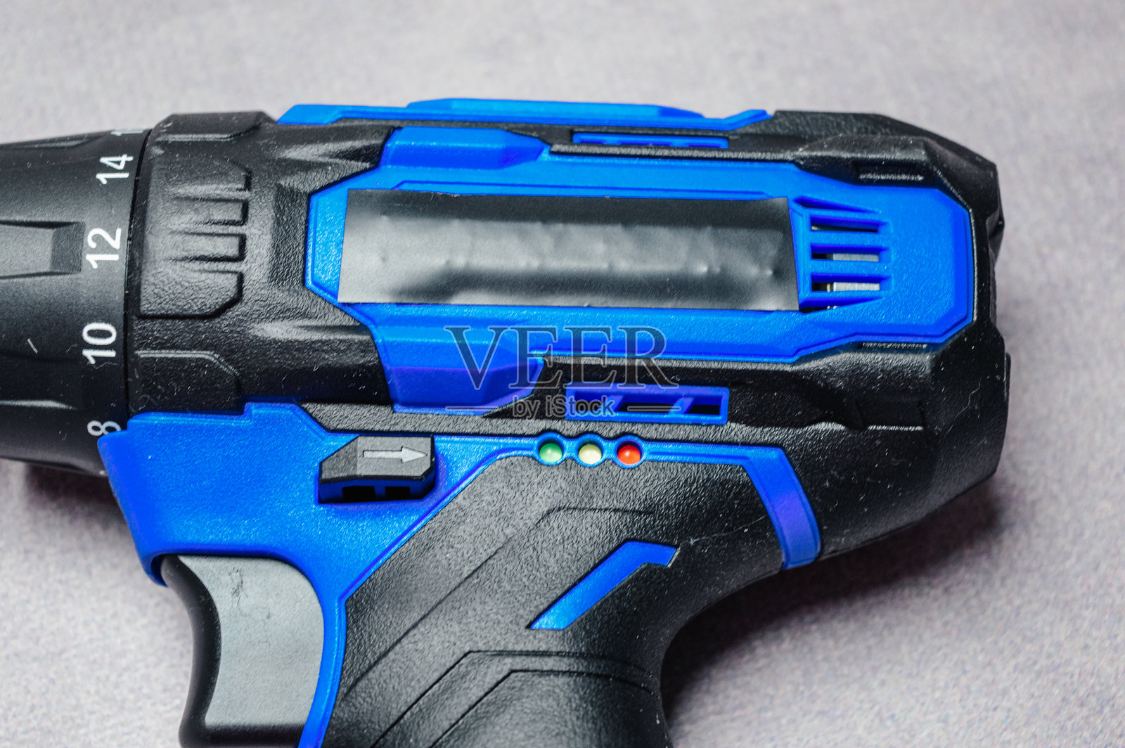 无绳电动钻手柄和夹头的特写，带有蓝色和黑色橡胶握把。现代电动工具上的触发器、扭矩设置和 LED 指示灯的详细视图。照片摄影图片