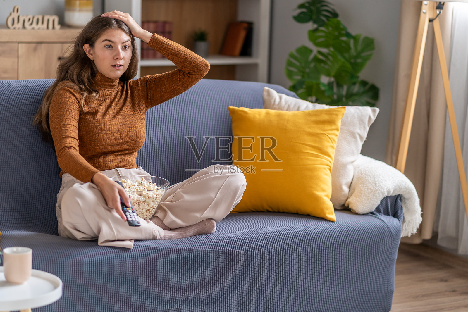 年轻女子在家中沙发上看电影，表情惊讶照片摄影图片