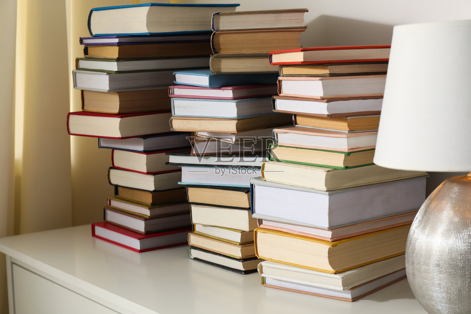 白色抽屉柜上的叠放的许多书籍和台灯，特写照片摄影图片