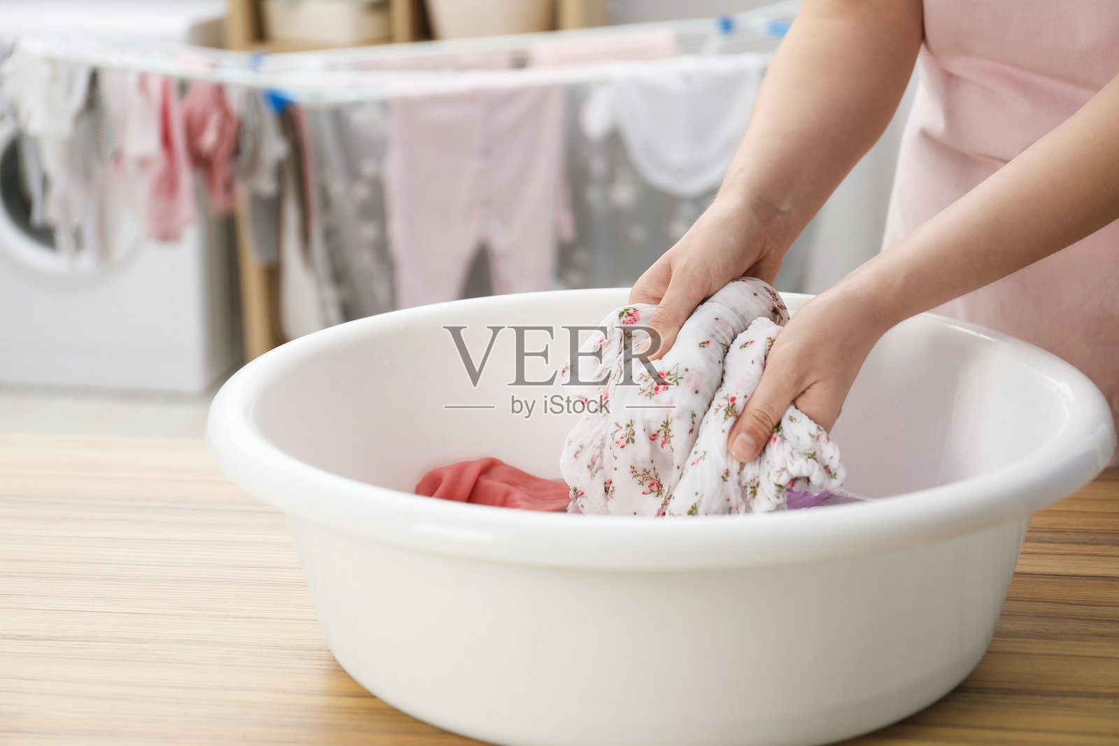 女人在室内木桌上的盆里洗婴儿衣服，特写照片摄影图片