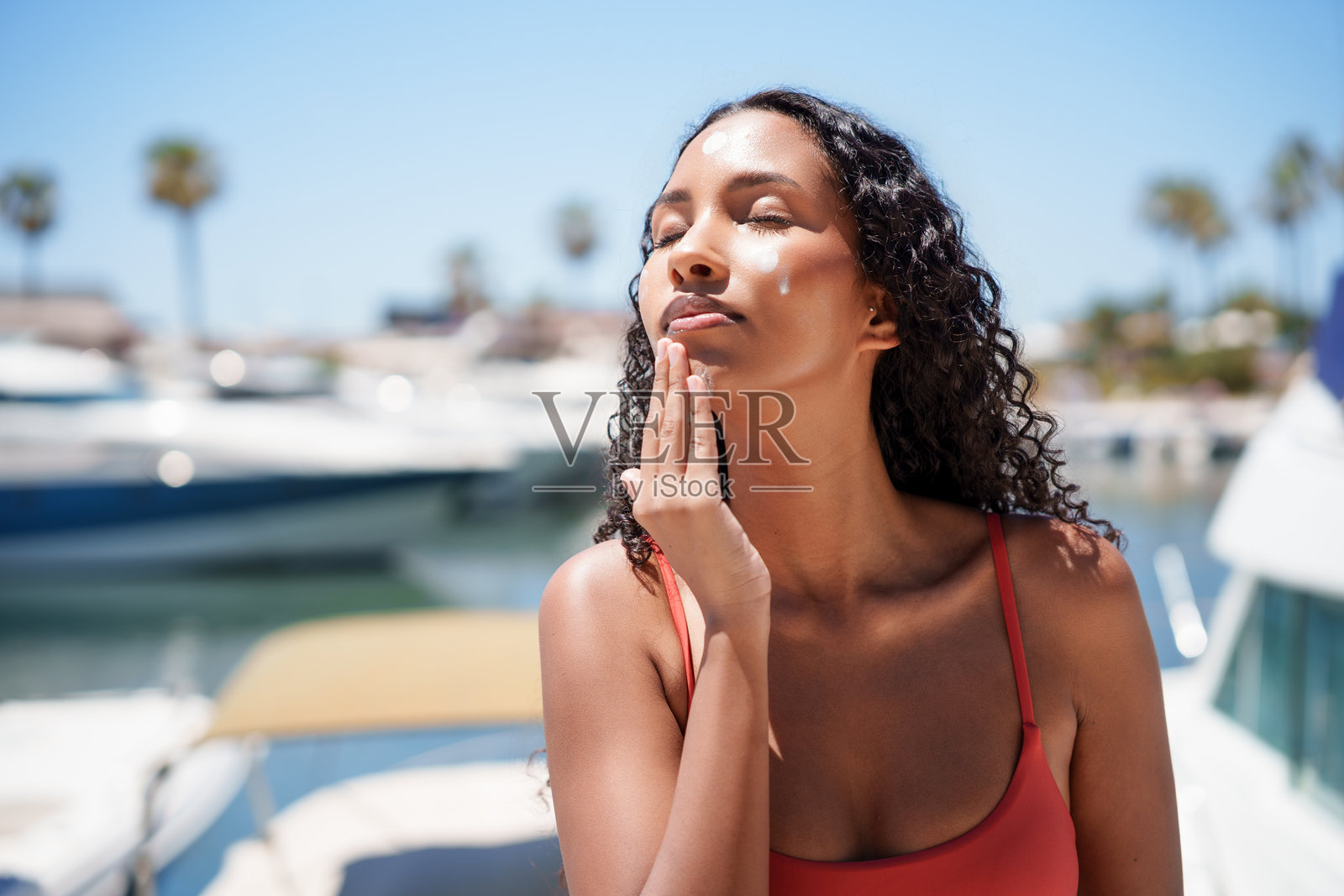 一位女士在停满船只的美丽码头边涂抹防晒霜照片摄影图片