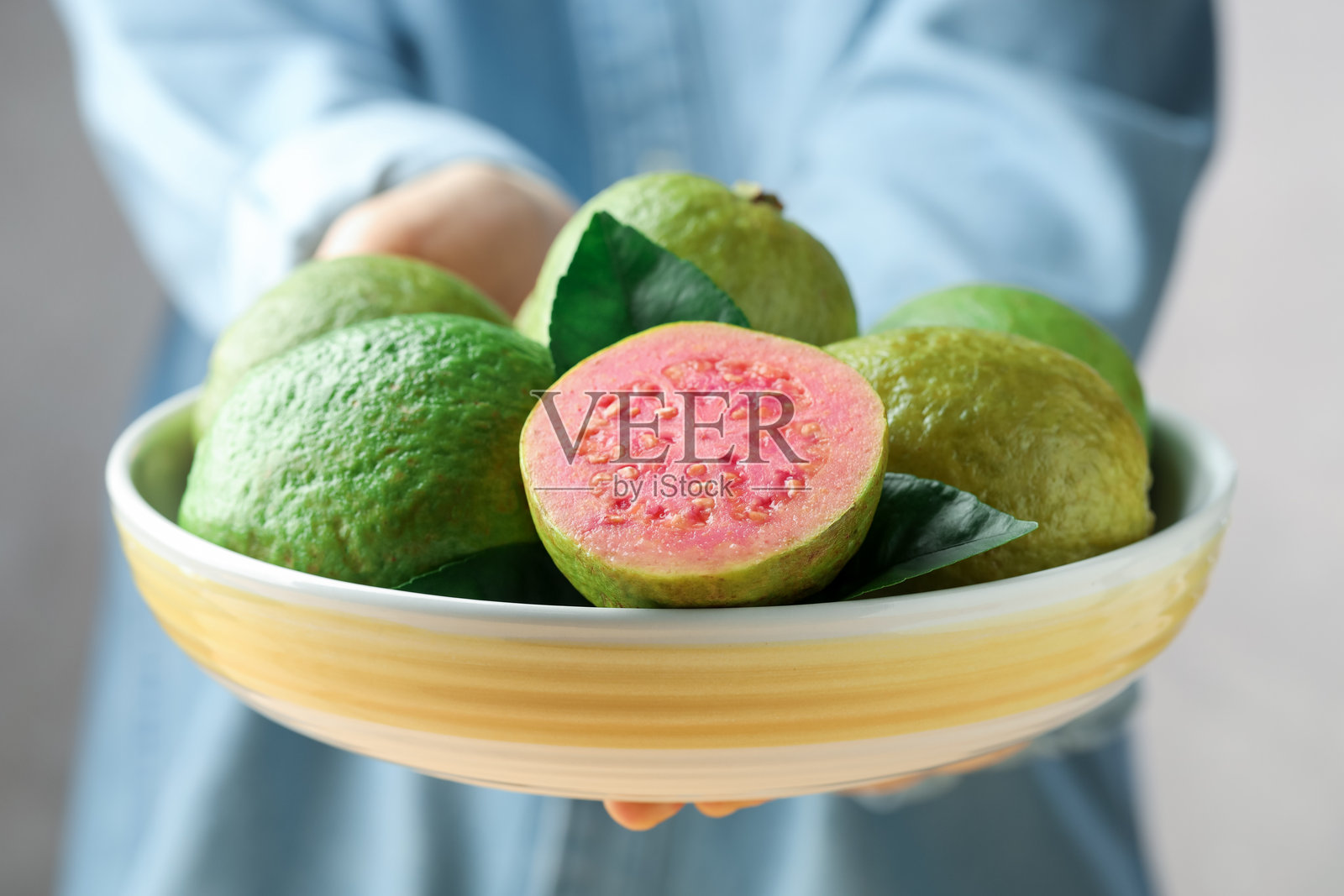 特写镜头：女子手捧一碗新鲜的番石榴，背景模糊。照片摄影图片