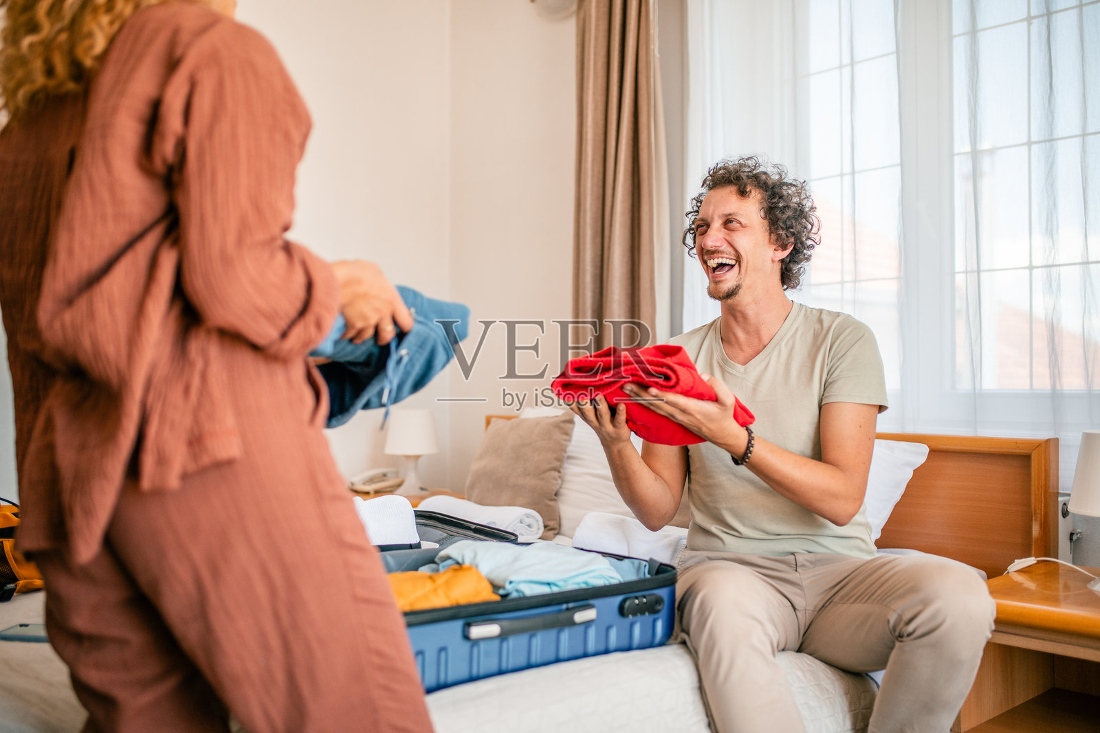 一对快乐恩爱的夫妇正坐在酒店房间的床上，整理着行李箱里的私人物品。照片摄影图片