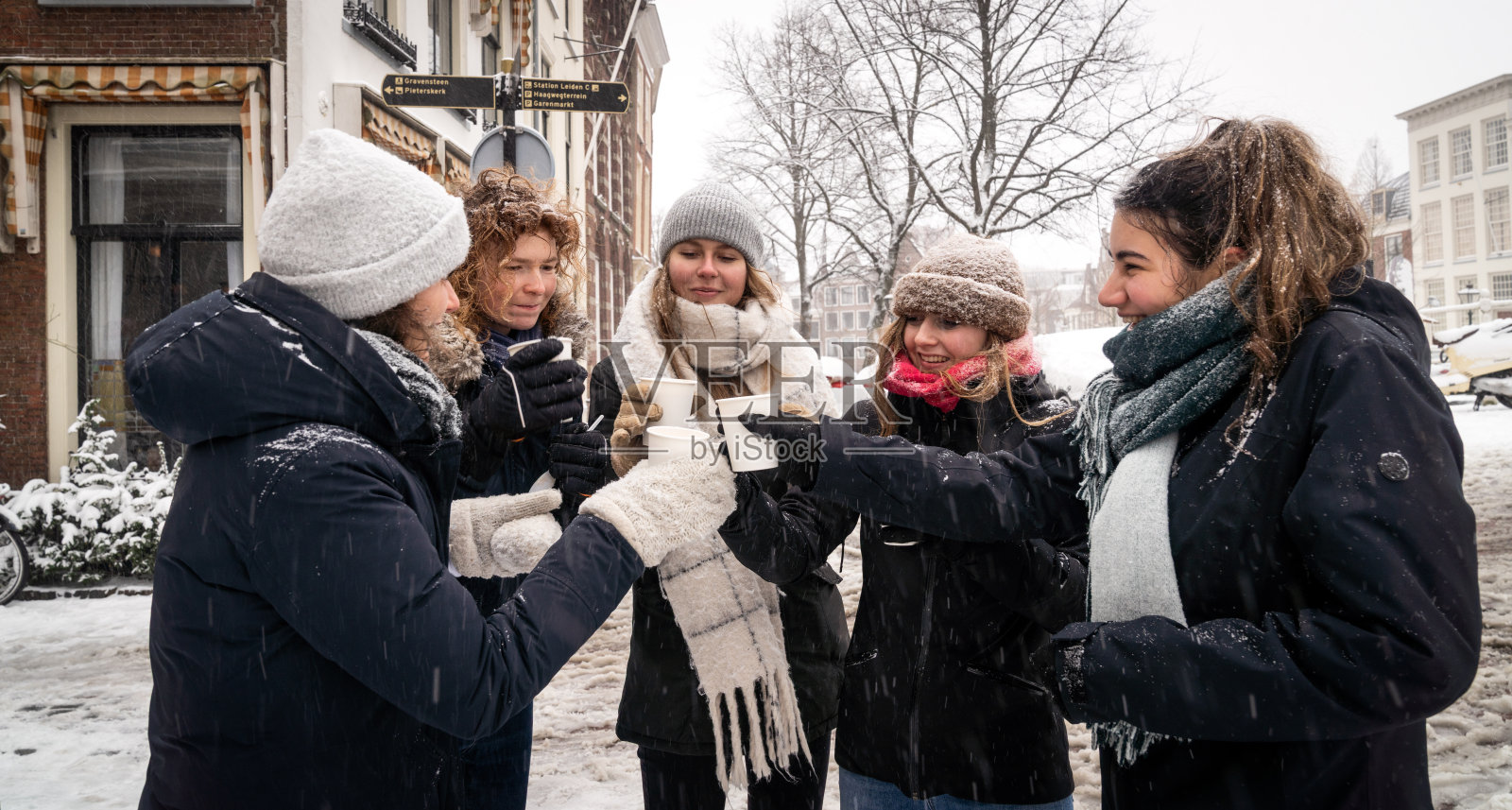 在下雪天，学生们在大学城莱顿的Rapenburg河边饮用热巧克力牛奶。照片摄影图片