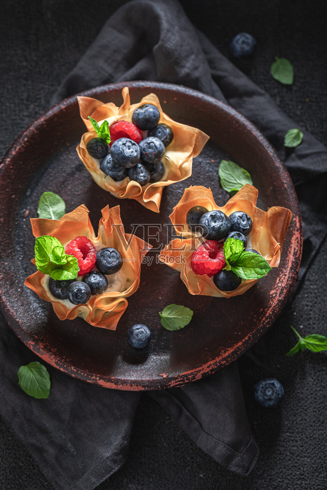 独特的、甜美的希腊酥皮杯，上面点缀着覆盆子和蓝莓。照片摄影图片
