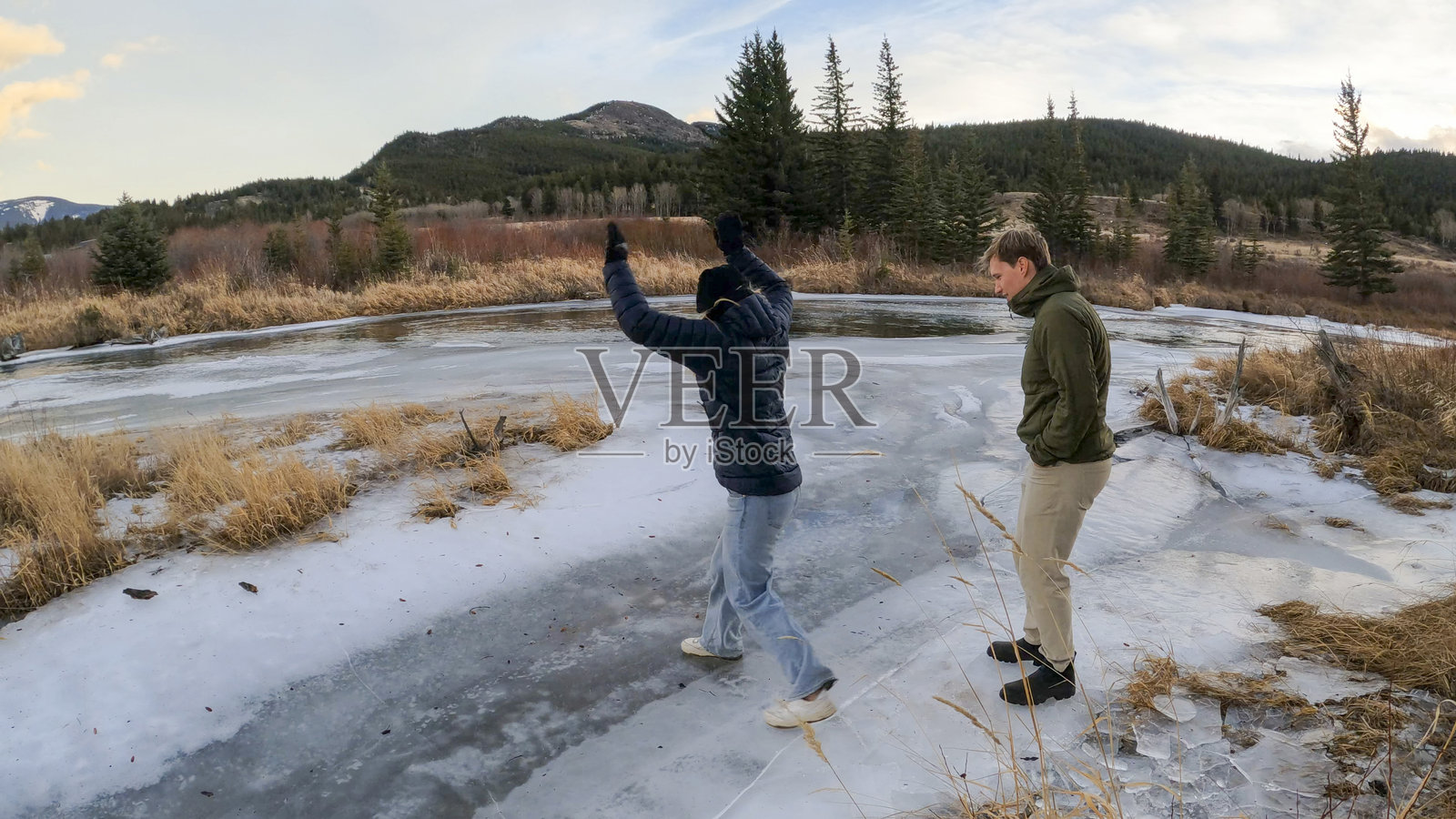 朋友们在冰封的河岸上玩耍，背景是加拿大落基山脉照片摄影图片