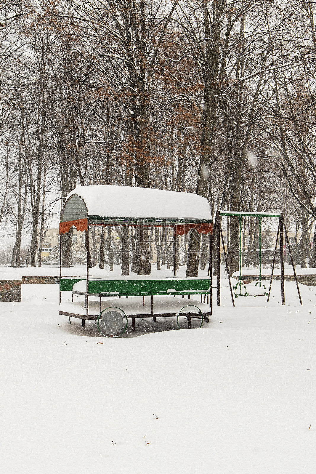 雪覆盖的攀爬架和秋千架在冬季的游乐场空荡荡地立着，映衬出寒冷季节里宁静和暂停的童年活动。照片摄影图片