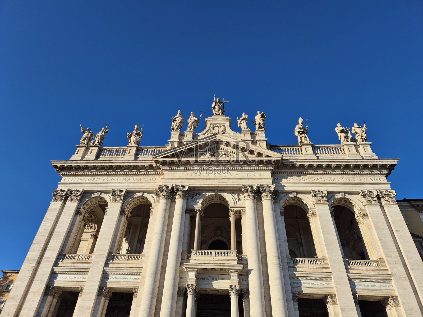 圣乔瓦尼·拉特兰诺教堂对称的正面拥有拱形入口、高耸的柱子以及屋顶沿线排列的圣徒雕像,这一切都沐浴在明亮的蓝天下。照片摄影图片
